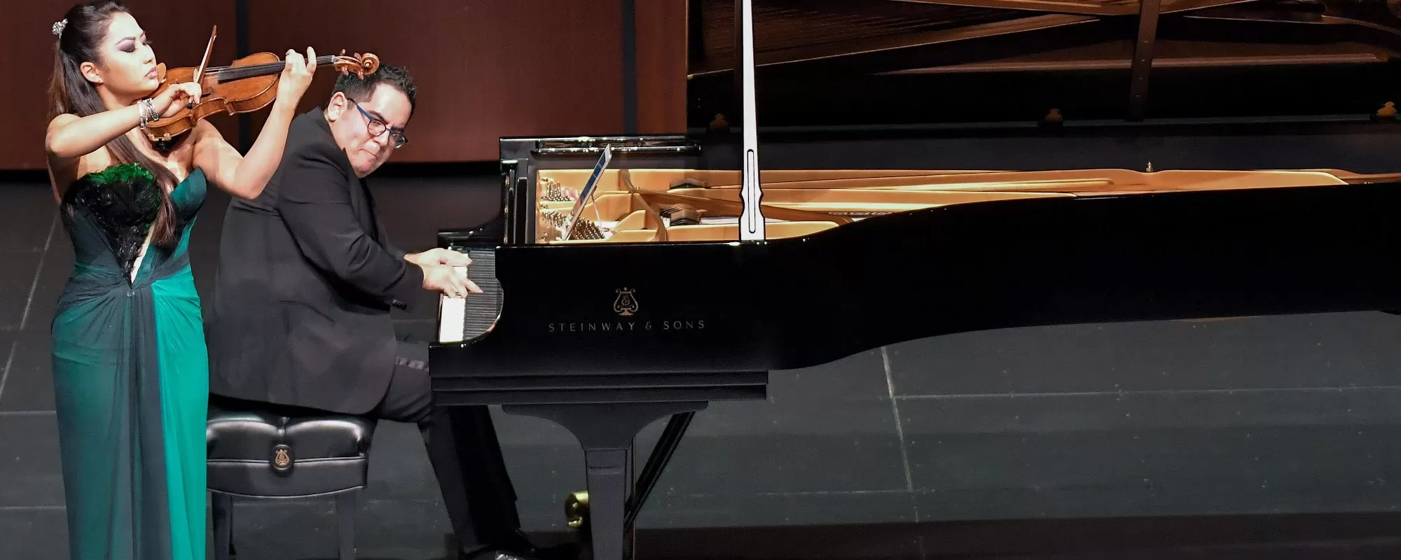 A woman in a green dress playing violin and a man playing a piano